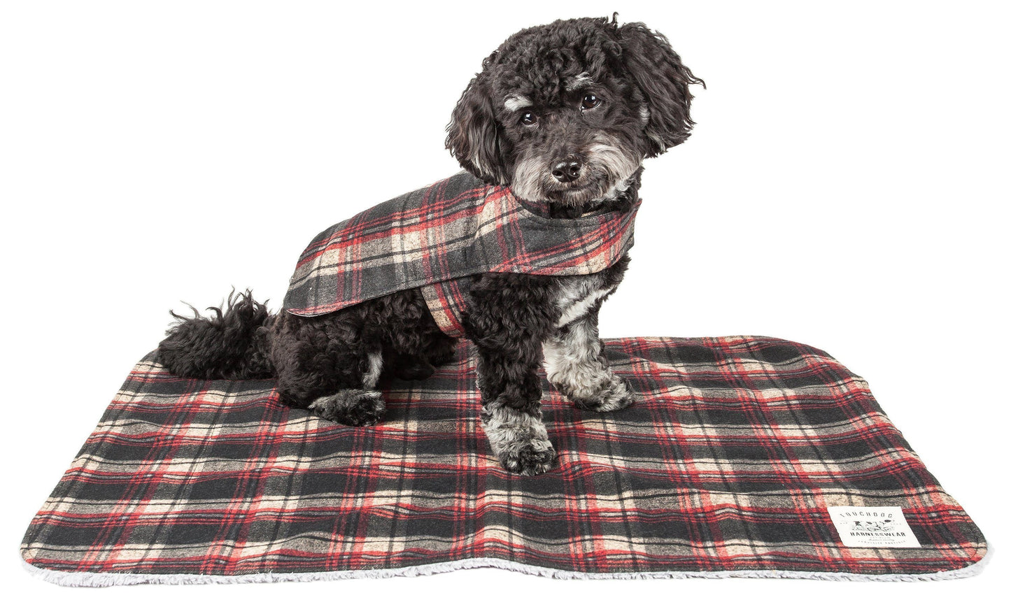 Dog wearing a plaid coat sitting on a matching plaid blanket.