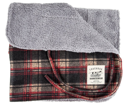 Folded blanket with gray fleece top and plaid pattern bottom, featuring a brand label.