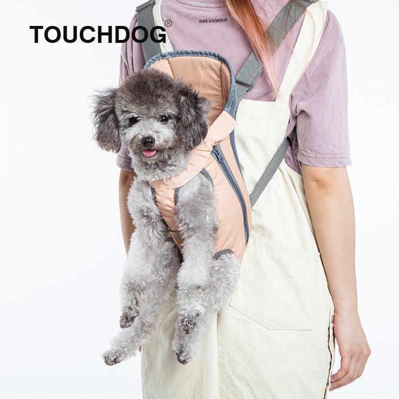 Small dog in a harness worn by a person with 'TOUCHDOG' branding