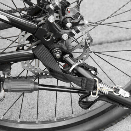 Close-up of a bicycle wheel with a strap and lock attached, on a pavement background.